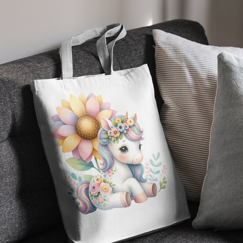 May include: A white tote bag with a colorful unicorn illustration. The unicorn is wearing a flower crown and is surrounded by flowers. The bag is made of canvas and has a white background.