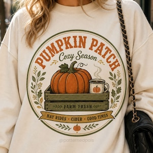 May include: A cream-colored sweatshirt featuring a circular graphic with the text PUMPKIN PATCH, Cozy Season, FARM FRESH, and HAY RIDES CIDER GOOD TIMES. The design includes an orange pumpkin in a wooden crate, a mug with steam, and foliage.