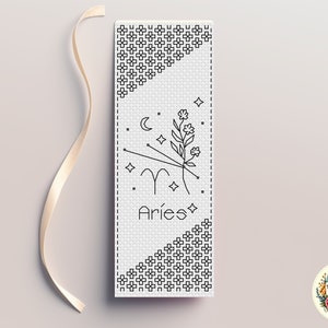 May include: Black and white cross stitch pattern for a bookmark featuring the zodiac sign Aries with a crescent moon, stars, and a floral design. The text "Aries" is below the design.