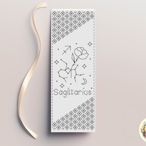 May include: Black and white cross stitch pattern for a bookmark featuring the Sagittarius zodiac sign with a flower and the text "Sagittarius".