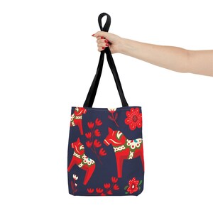 May include: A navy blue tote bag with a repeating pattern of red and white Dala horses and red flowers. The bag has black straps.