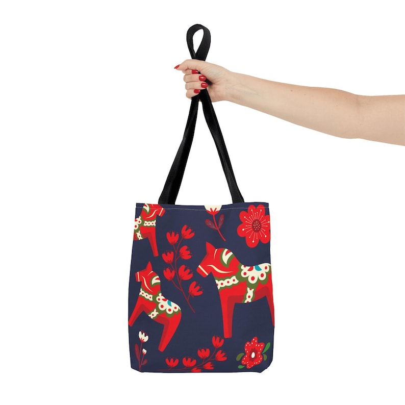 May include: A navy blue tote bag with a repeating pattern of red and white Dala horses and red flowers. The bag has black straps.