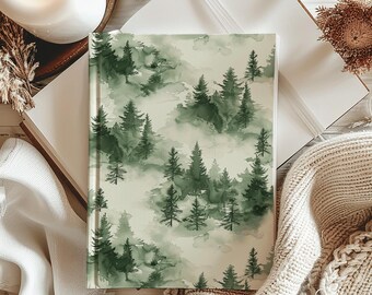 May include: A green and white watercolor journal with a forest scene featuring trees and clouds. The journal is lying on a white surface with a brown knitted blanket and a candle.