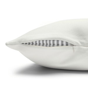 May include: A white pillow with a zipper closure. The zipper is open, revealing a gray and white striped fabric lining.