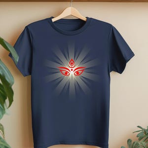 May include: Navy blue t-shirt with a red and white graphic of a deity's eyes and forehead. The design has a radial pattern. The shirt is displayed on a wooden hanger.