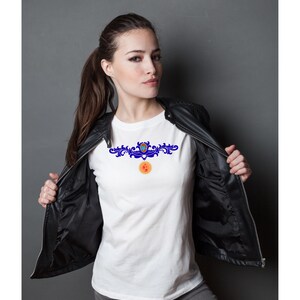 May include: A white t-shirt with a blue and orange decorative design. The design is centered on the chest. The person is wearing a black leather jacket and grey trousers. The background is a solid grey.