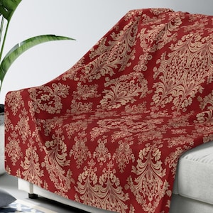 May include: A red throw blanket with a beige damask pattern. The blanket is draped over a white couch.
