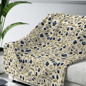 May include: A cream-colored throw blanket with a navy blue and gray floral pattern. The blanket is draped over a white couch.
