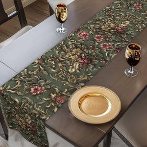 May include: A dining table set for a meal, featuring a green floral table runner, gold-rimmed wine glasses, and a gold plate. The table is surrounded by dark wooden chairs, with a festive garland in the background.