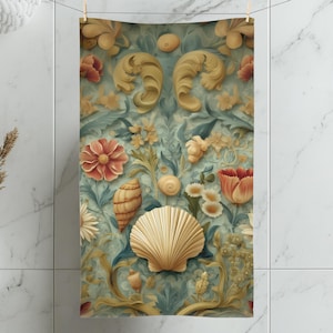 May include: A decorative towel with a floral and seashell design. The towel features a light blue background with detailed illustrations of flowers, seashells, and ornate scrollwork in shades of red, yellow, and gold. The towel is hanging on a clothesline.