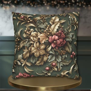 May include: Square decorative pillow with a floral design in shades of green, gold, and red. The pillow features a detailed pattern of flowers, leaves, and berries. The pillow is placed on a gold-colored table.