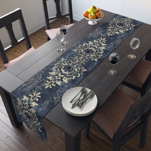 May include: A blue and gold damask table runner with a distressed look. The runner is placed on a dark wood table with two chairs and a set of white plates and silverware.