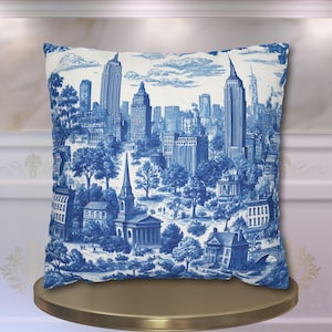 May include: Square throw pillow with a blue and white toile design featuring a detailed illustration of the New York City skyline. The pillow showcases iconic buildings, trees, and a bridge, creating a classic decorative piece.