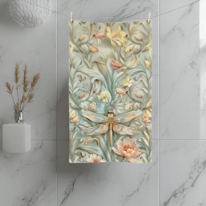 May include: A rectangular towel featuring a detailed dragonfly centered over a soft-toned botanical pattern. The design includes pale yellow, peach, and sage green floral elements with swirling vines against a light, muted background.