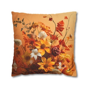 Könnte beinhalten: Quadratisches Kissen mit einem Blumendesign in Orange-, Gelb- und Weißtönen. Das Bild zeigt eine detaillierte Illustration von Blumen und Blättern, die eine weiche und einladende Ästhetik erzeugt.