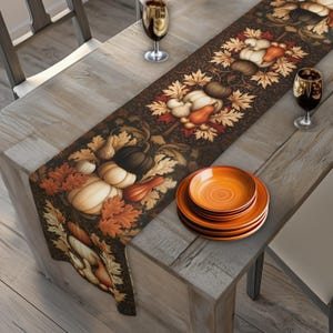 May include: A rectangular table runner featuring a repeating pattern of pumpkins, gourds, and autumn leaves in shades of orange, brown, and cream on a dark background, displayed on a wooden table with a stack of orange plates and two wine glasses.