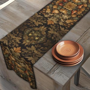 May include: A table runner with a dark background and a detailed floral and foliage pattern in gold, brown, and orange. A stack of orange-brown plates sits on a wooden table.