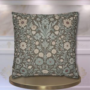 May include: Square decorative pillow with a floral pattern in shades of gray, cream, and blue. The design features stylized flowers and foliage, creating a vintage or botanical aesthetic. The pillow is likely made of fabric.