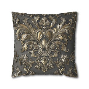 May include: Square cushion with a detailed gold and grey baroque design. The cushion features a raised, ornate pattern of swirling leaves, flowers, and scrollwork against a dark grey background. The design is symmetrical and centered.
