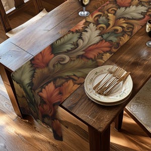 May include: A long table runner featuring a repeating pattern of stylized acanthus leaves in shades of burnt orange, sage green, and cream. The runner is placed on a dark wooden table with a stack of white plates, a fork, and a knife.