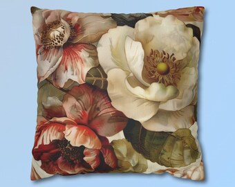 May include: A square throw pillow featuring a detailed floral print with large, overlapping blossoms in shades of cream, soft white, deep red, and muted orange. The design includes dark green foliage and intricate petal textures across the fabric surface.
