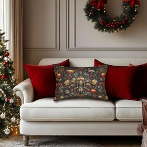 May include: A rectangular throw pillow featuring a dark, intricate pattern of a central nutcracker figure surrounded by red apples, pinecones, green foliage, and small pies against a dark background, positioned between two solid red pillows.
