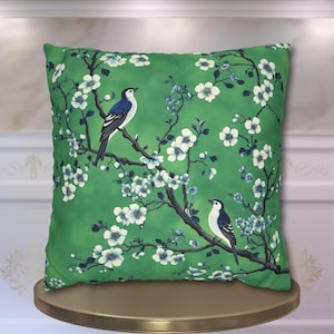 May include: Green cushion with a floral pattern and two blue birds perched on branches. The cushion has a white background with green leaves and white flowers.