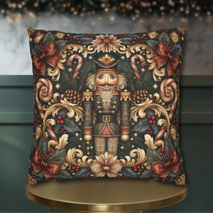 May include: A square throw pillow featuring a central nutcracker figure in a dark blue uniform with gold accents. The design includes ornate gold scrollwork, red bows, candy canes, pine cones, and holly berries on a dark background.