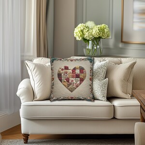 May include: A square throw cushion featuring a cream-coloured quilted fabric base with a central heart-shaped patch made of multi-coloured floral and checkered fabric squares, framed by a decorative border of embroidered leaves and flowers.