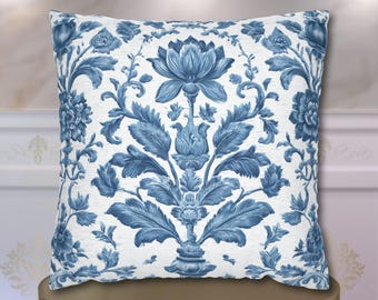 May include: A square throw pillow featuring a white background with a symmetrical blue floral pattern. The design displays a central large flower surrounded by intricate leafy stems and smaller blossoms, creating a detailed botanical motif.