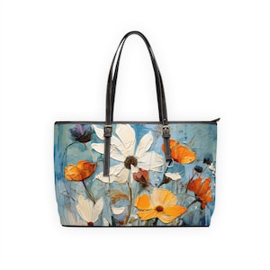 May include: A blue tote bag with a floral print featuring white, orange, and yellow flowers. The bag has black leather handles and a zip closure.