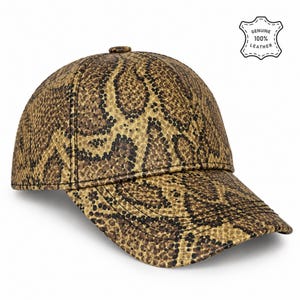 May include: A baseball cap featuring a brown and black snakeskin pattern. The cap has a structured crown, a curved brim, and a small button at the top. A white label in the upper right corner displays the text: GENUINE 100% LEATHER.