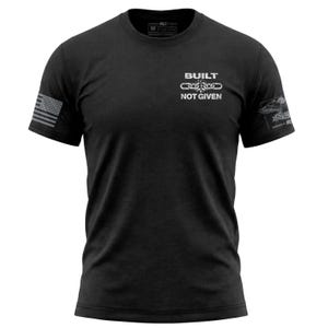 Può includere: Una t-shirt nera a maniche corte con girocollo, caratterizzata dalla scritta bianca BUILT NOT GIVEN e dal grafico di una catena spezzata sul petto. La manica destra mostra una bandiera americana grigia, la sinistra un emblema d'aquila.