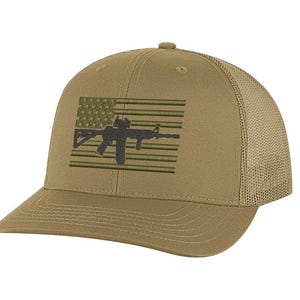 Peut inclure: Une casquette de baseball de style trucker beige avec un motif brodé sur le panneau avant. La broderie représente un drapeau américain stylisé en vert olive, superposé d'une silhouette gris anthracite d'un fusil de type AR-15.