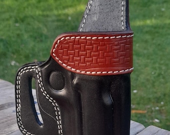 Könnte beinhalten: Eine schwarze Lederholster mit weißen Nähten. Die Holster hat ein braunes, strukturiertes Band mit weißen Nähten. Die Holster ist für das Tragen an der Hüfte konzipiert. Die Holster ist aus Leder.