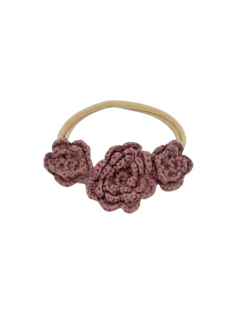 May include: A mauve crochet headband featuring three flower accents. The flowers are made of a textured yarn and are attached to a neutral-colored elastic band. This handmade accessory is suitable for babies and young children.