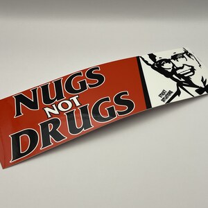 May include: Red and white sticker with the text "NUGS NOT DRUGS" in black lettering. The sticker features a black and white silhouette of Colonel Sanders.