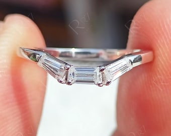 May include: A silver-toned metal ring featuring a chevron-shaped band set with three clear baguette-cut stones. The center stone is a rectangular baguette, flanked by two smaller, slightly angled baguette-cut stones, all held in a prong setting.