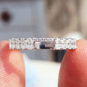 May include: A silver-toned band ring featuring a row of rectangular baguette-cut stones along the sides and a small gap at the top, which is accented with a thin line of tiny, round, clear stones set into the metal band.