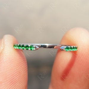 Op de afbeelding: Een zilveren ring met een rij kleine groene edelstenen aan elke kant.