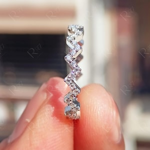 May include: A delicate silver band ring with a zig-zag pattern of small, clear diamonds.