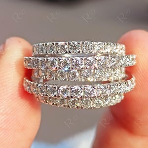 May include: A multi-row ring crafted from polished silver-toned metal, featuring four distinct bands connected together. Each band is densely set with numerous small, round, clear faceted stones that create a continuous sparkling effect.