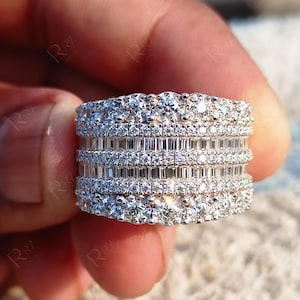 May include: A wide silver band ring with multiple rows of sparkling diamonds. The ring features a combination of round and baguette-shaped diamonds.