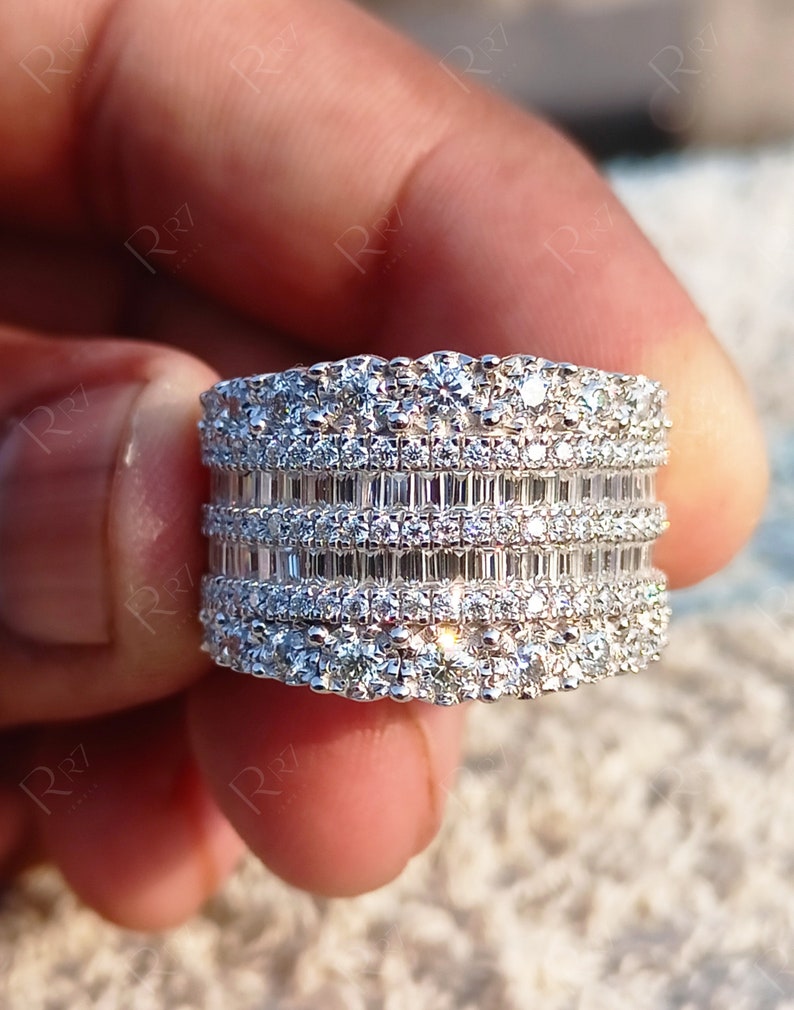 May include: A wide silver band ring with multiple rows of sparkling diamonds. The ring features a combination of round and baguette-shaped diamonds.