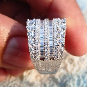 May include: A silver ring with a wide band featuring multiple rows of baguette and round cut diamonds.