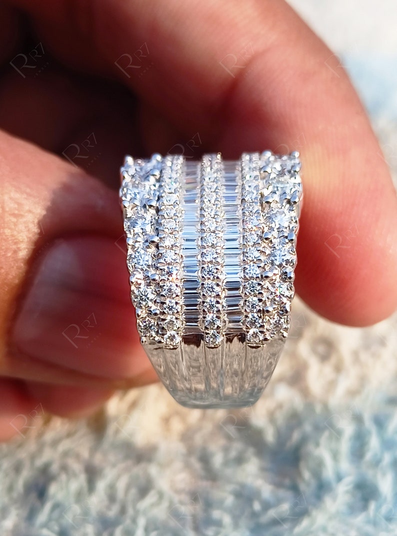 May include: A silver ring with a wide band featuring multiple rows of baguette and round cut diamonds.