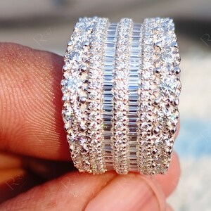 May include: A wide silver band ring with multiple rows of sparkling diamonds. The ring features a combination of round and baguette-cut diamonds.
