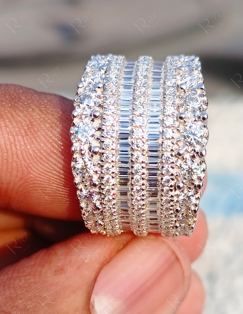 May include: A wide silver band ring with multiple rows of sparkling diamonds. The ring features a combination of round and baguette-cut diamonds.