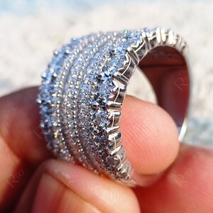 May include: A silver band ring with multiple rows of small, clear cubic zirconia stones.