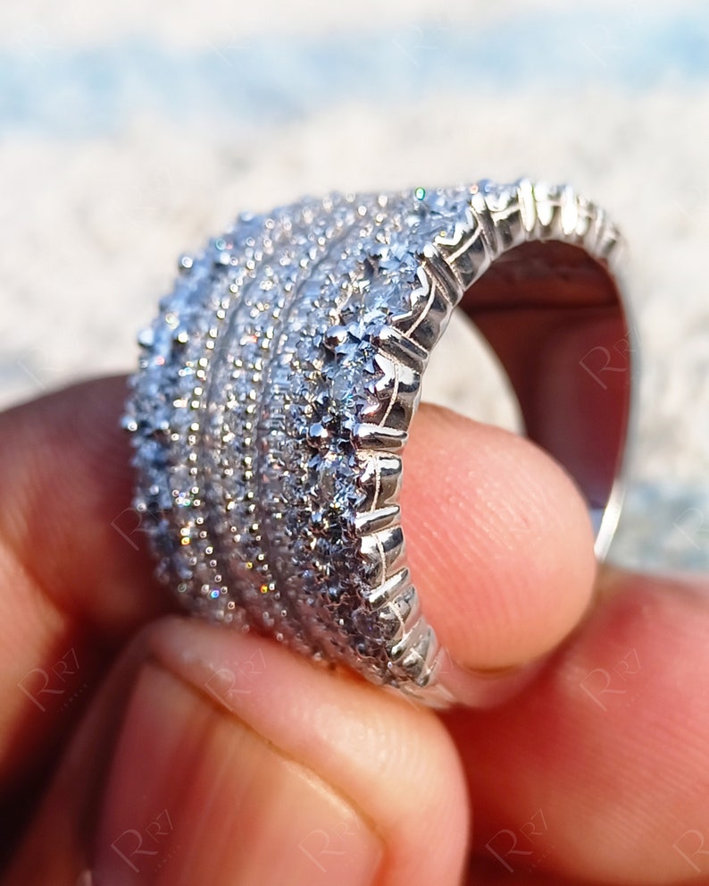 May include: A silver band ring with multiple rows of small, clear cubic zirconia stones.